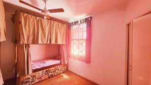 Une chambre avec un lit superposé, un ventilateur de plafond, une fenêtre avec des rideaux à motifs et une porte.