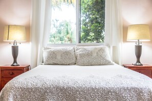 A neatly made bed with patterned bedding, two bedside lamps, and a window with curtains. - Mayan Villas Hotel (Chiquilá)