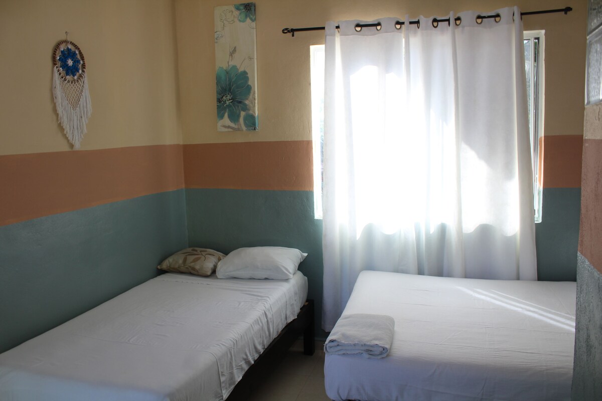 A room with two single beds, a wall hanging, and a window with curtains.