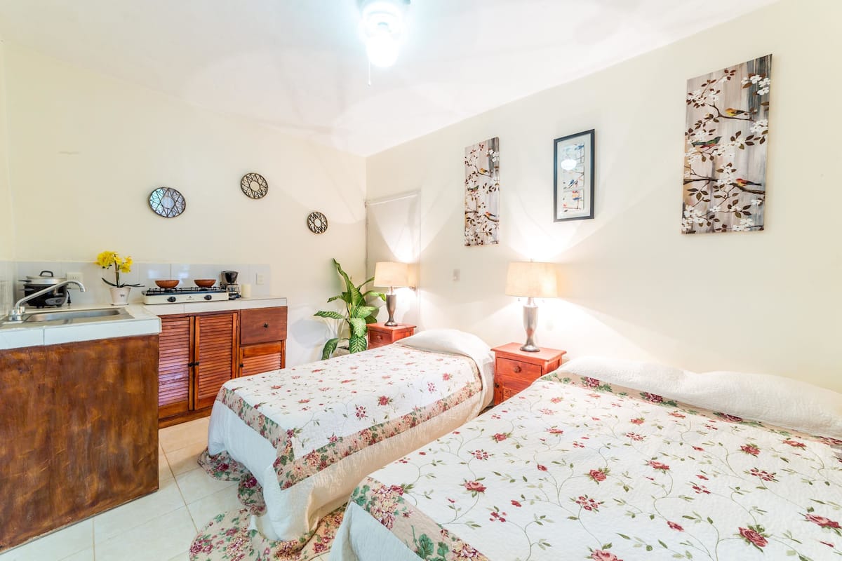 Un dormitorio con dos camas, una kitchenette pequeña y un baño.