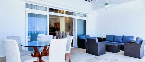 A modern outdoor dining area with a glass table and wicker chairs, adjacent to a blue sofa and wicker lounge chairs.