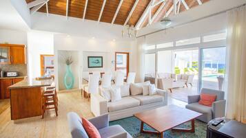 A spacious living area with a wooden ceiling, a large window with a view, and a kitchen area with wooden cabinets.