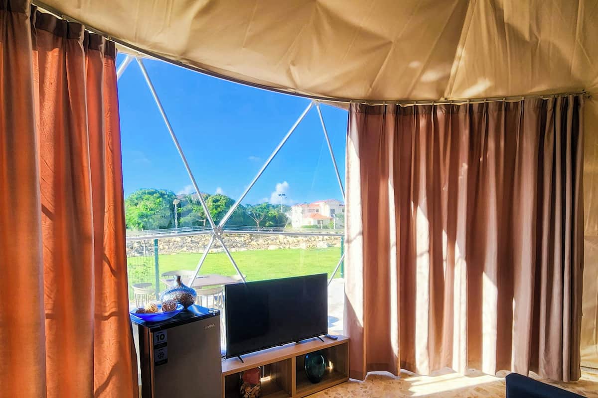 A tented room with a television, sofa, and a view of a green landscape.