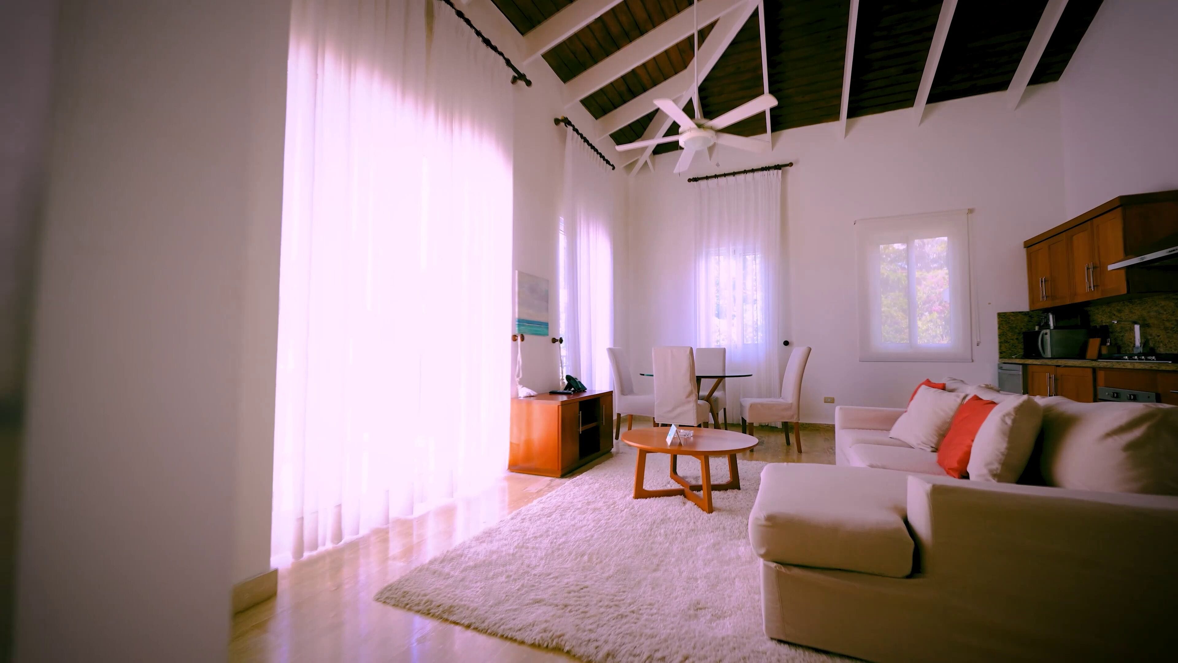 A spacious living room with a high ceiling, large windows, a sofa, a coffee table, and a kitchen area.