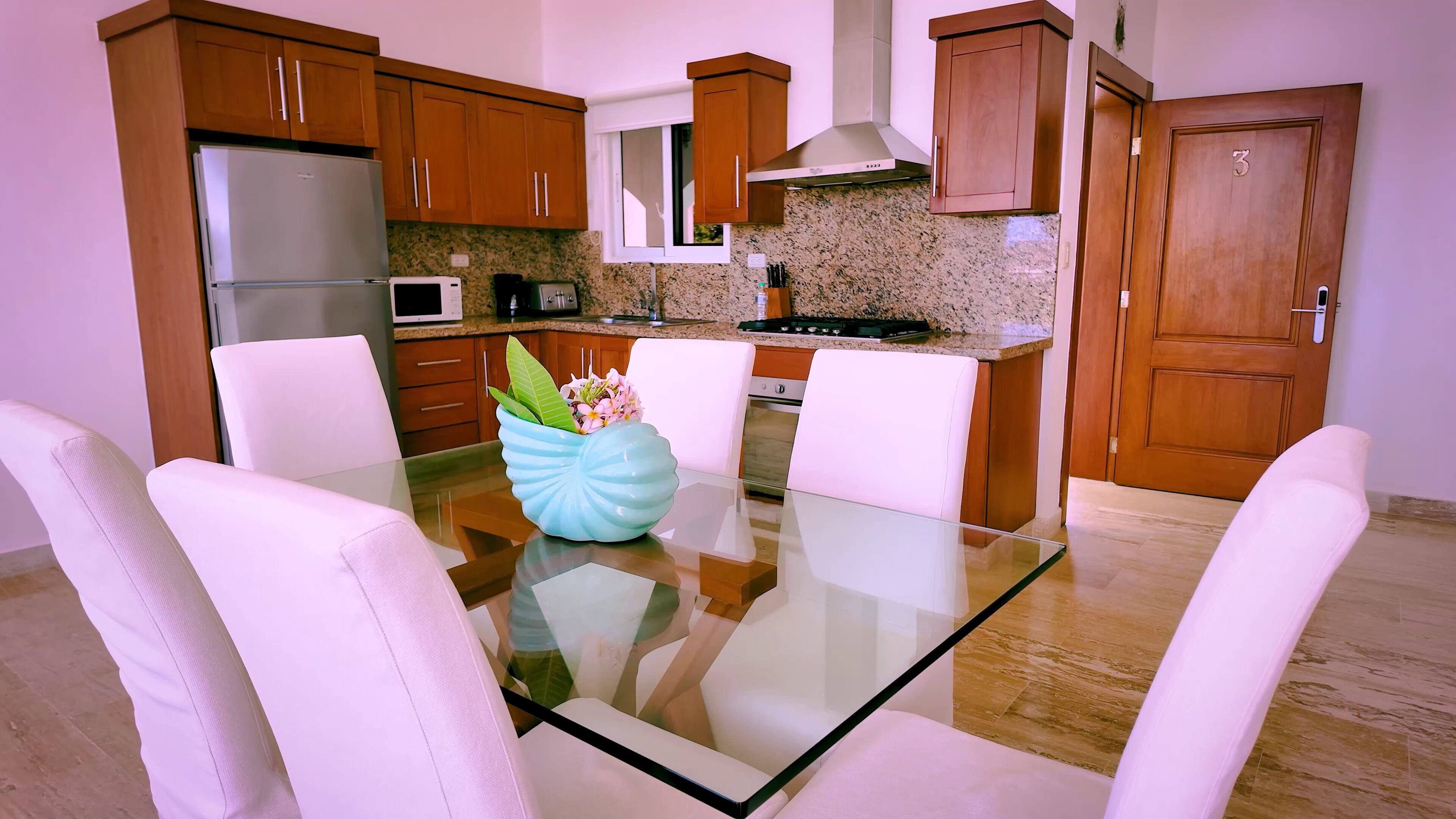 A modern kitchen with wooden cabinets, a glass dining table, and white chairs.