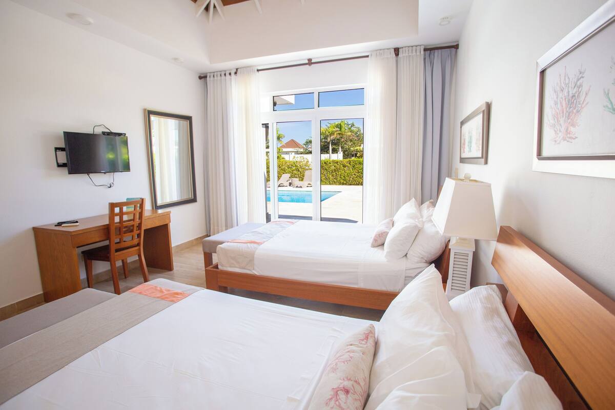 A hotel room with two beds, a desk, a chair, a TV, and a view of a swimming pool.