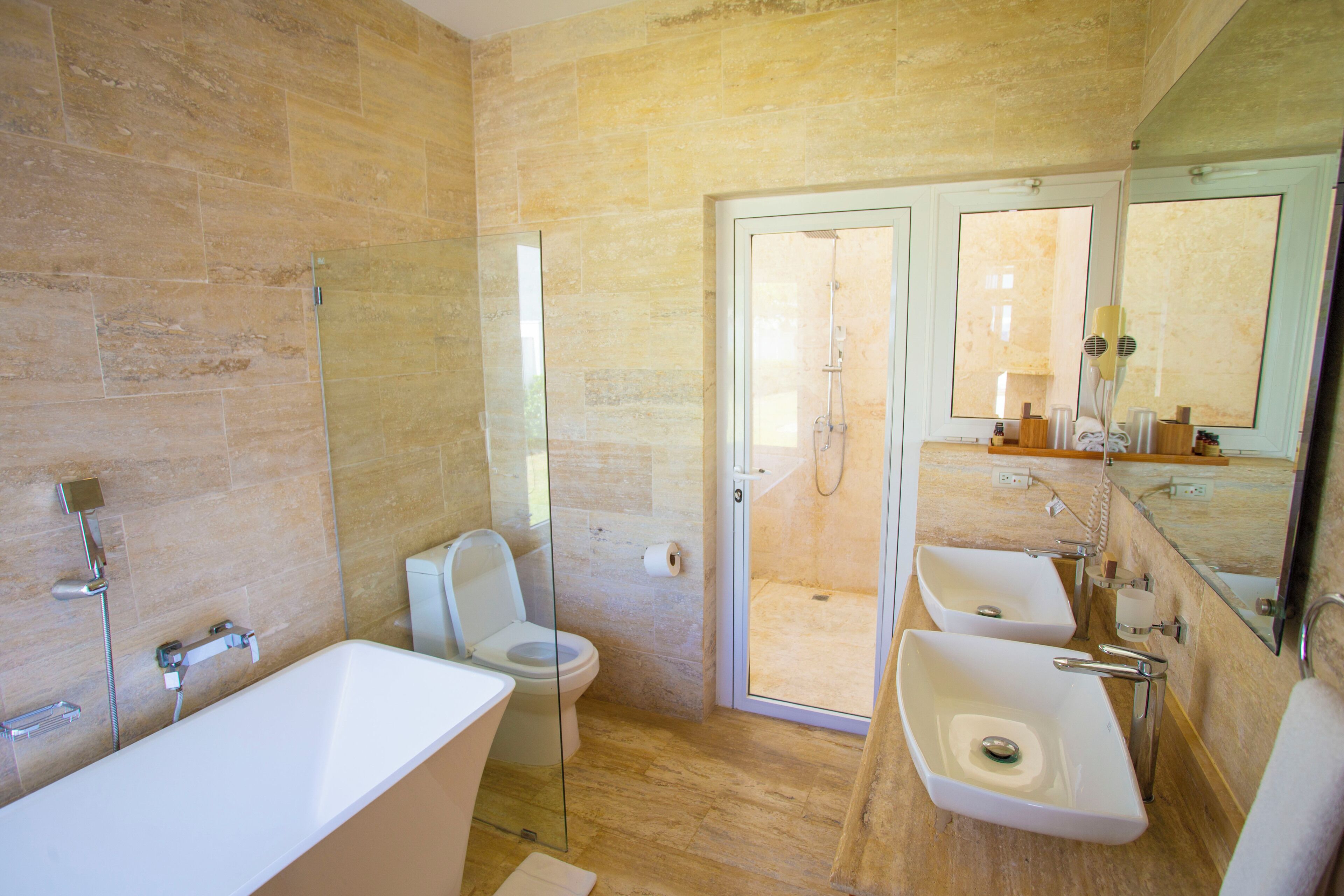 Un baño moderno con bañera, dos lavamanos, inodoro y cabina de ducha con mampara de cristal.