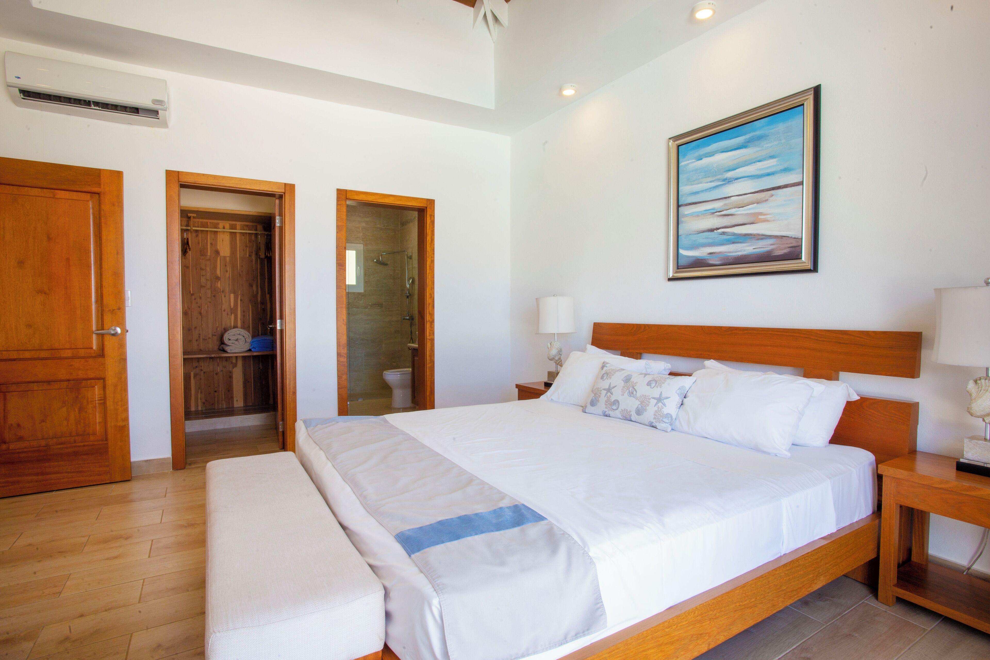 A spacious bedroom with a large bed, wooden headboard, and a painting on the wall.