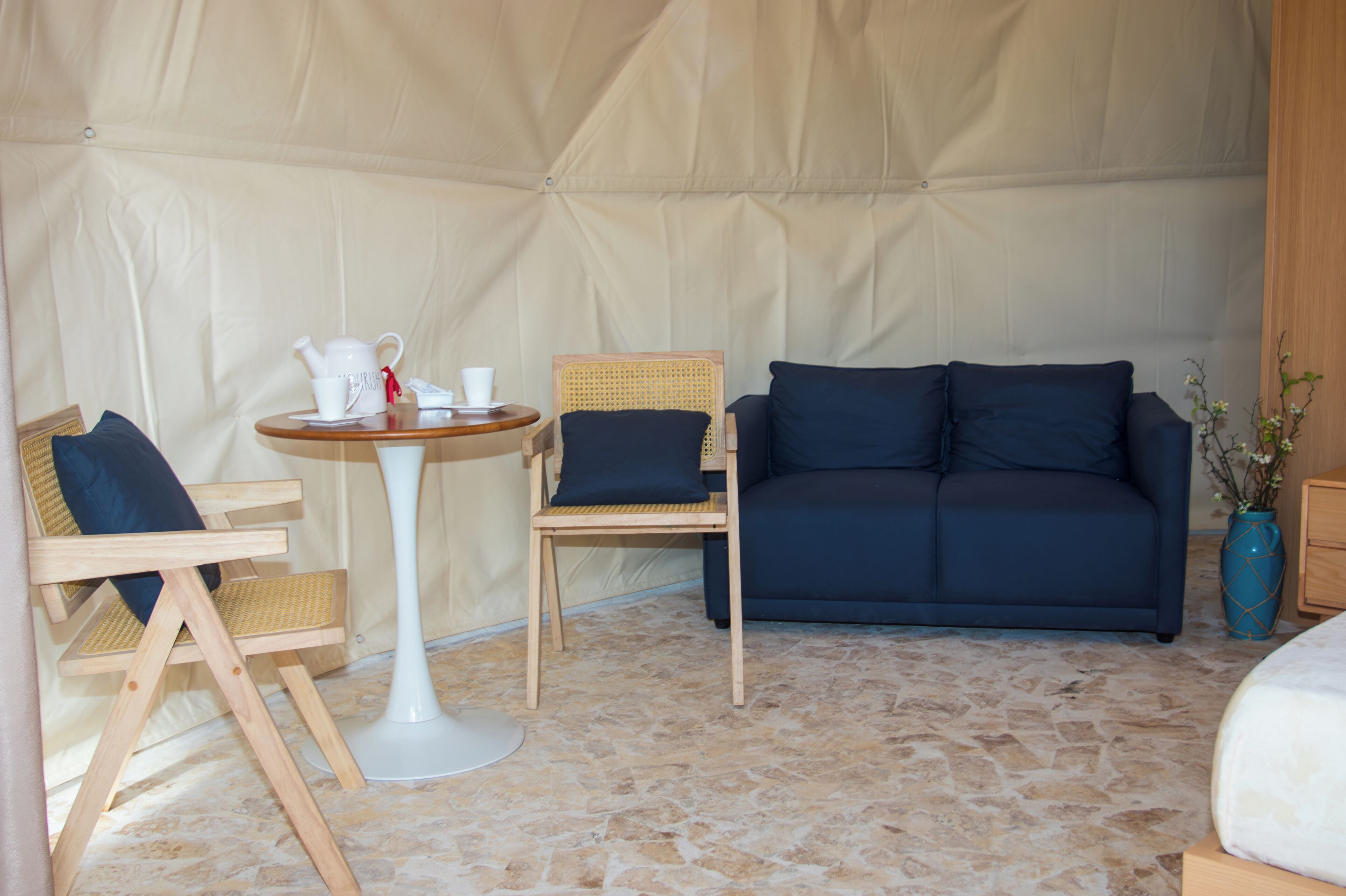 A tented room with a white table, two chairs, a dark blue sofa, and a vase with flowers.