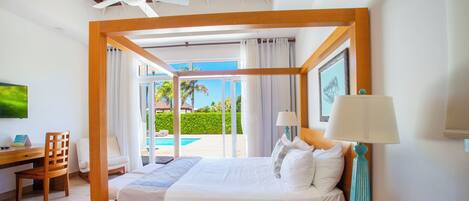 A spacious bedroom with a large bed, a desk, and a chair, featuring a view of a pool and greenery.