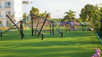 Un parque infantil con estructuras para escalar y un tobogán, rodeado de césped y árboles.
