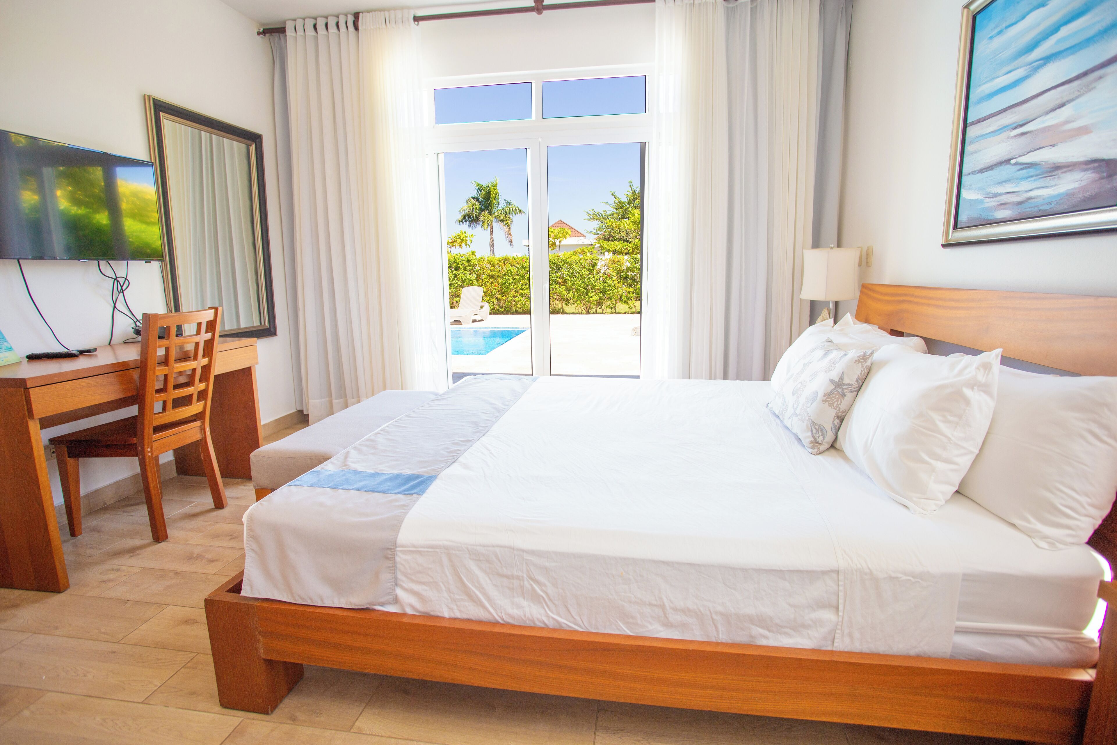Une chambre d’hôtel équipée d’un lit, d’un bureau, d’une chaise, d’une télévision et offrant une vue sur une piscine et un espace verdoyant.