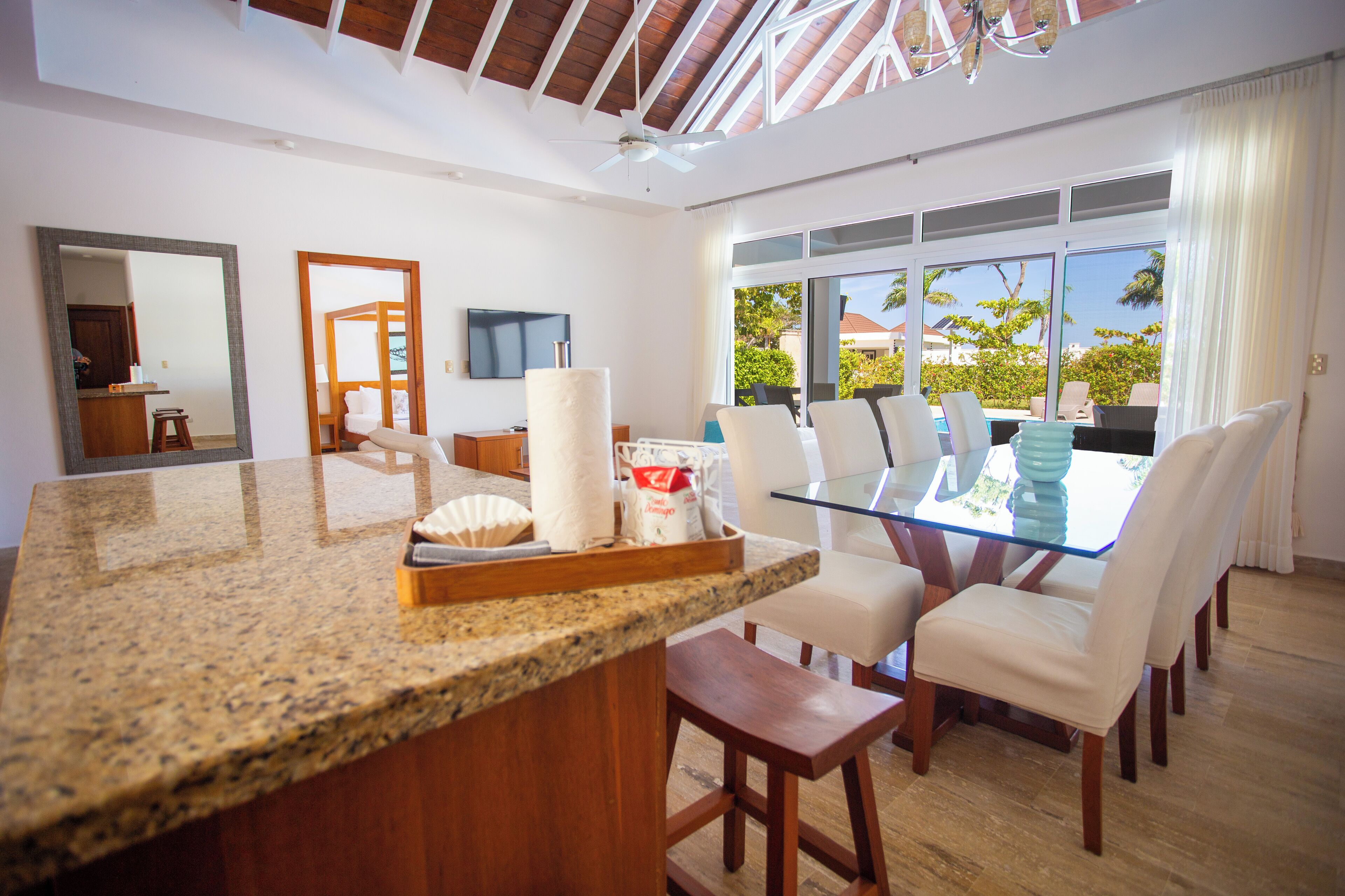 A modern kitchen with granite countertops, a glass dining table, and white chairs.
