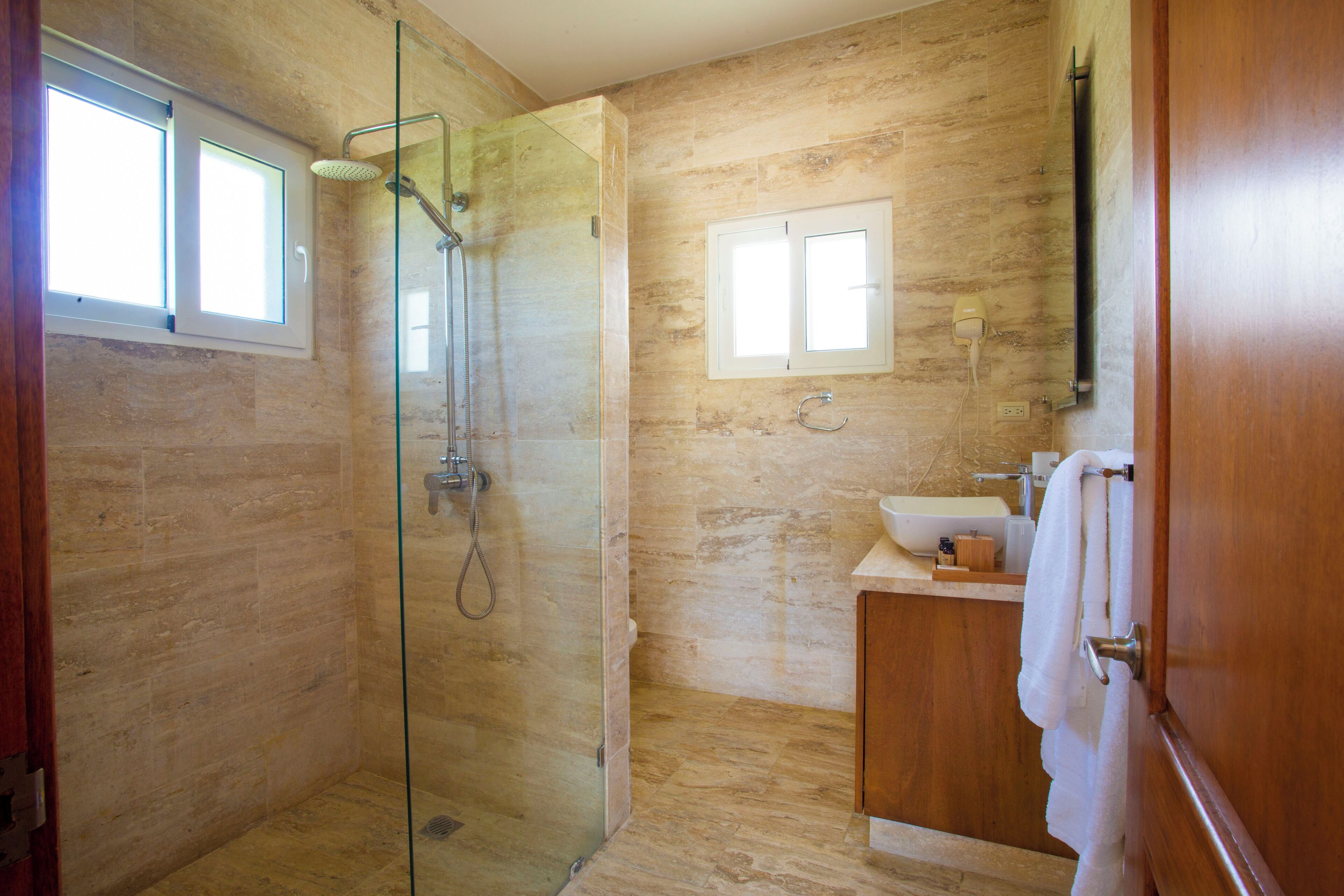A modern bathroom with a glass-enclosed shower, a wooden vanity, and a window providing natural light.