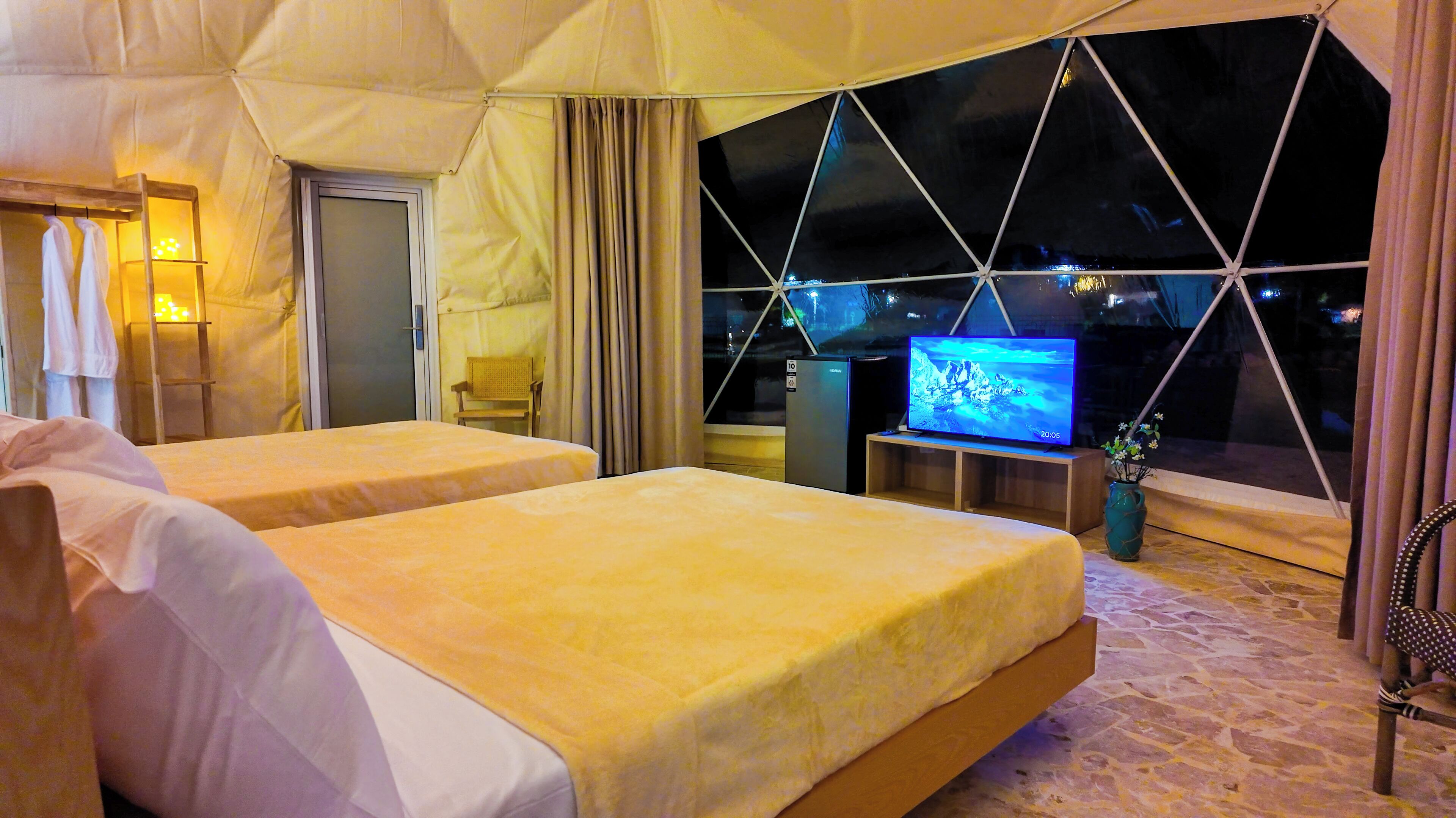 A room with two beds, a television, and a window with a view of the night sky.