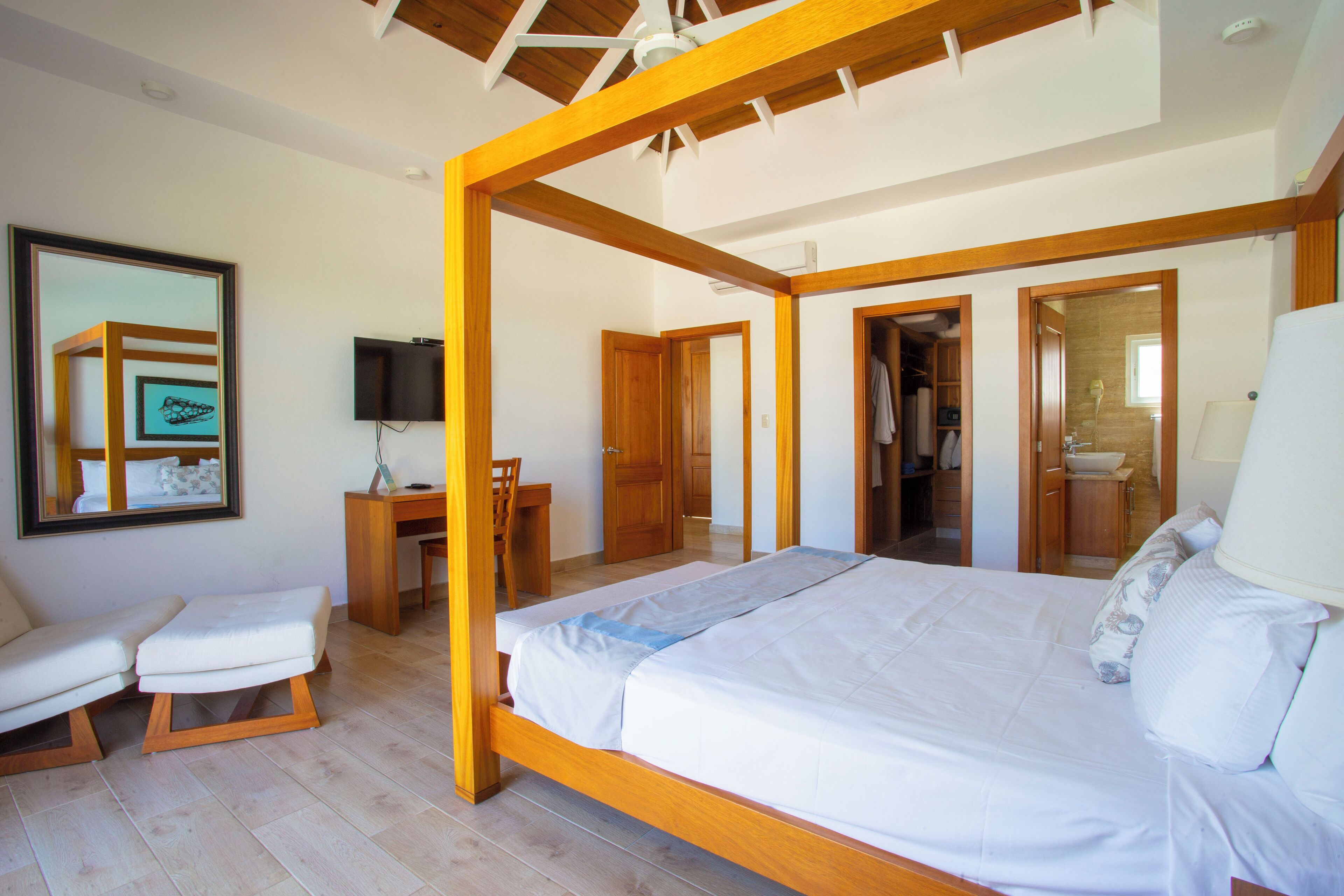 A bedroom with a wooden four-poster bed, a desk, a chair, and a television.