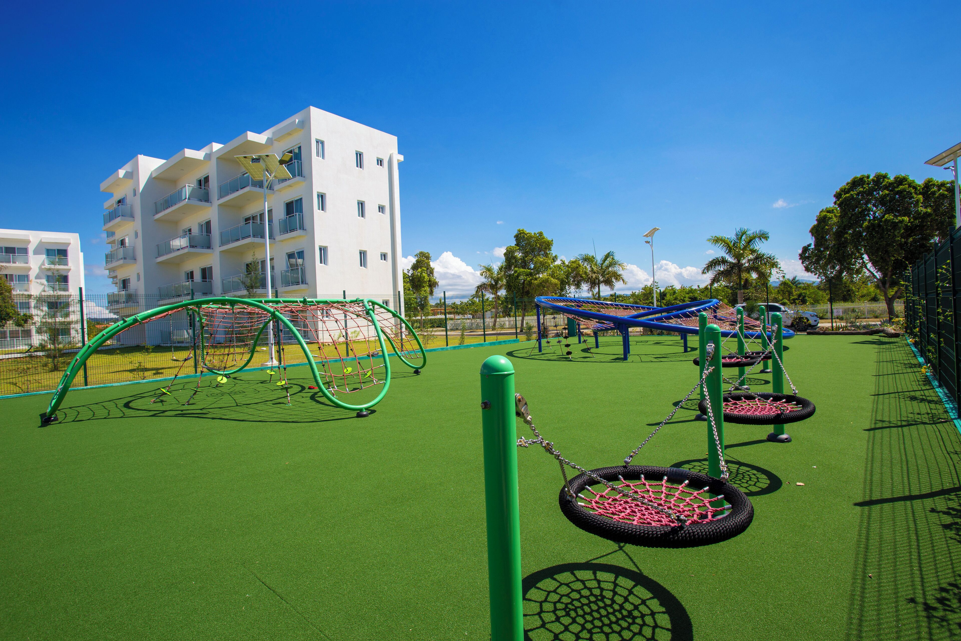 Ein Spielplatz mit grüner Gummibeschichtung, Reifenkarussells und einer Kletterzone mit Netz.
