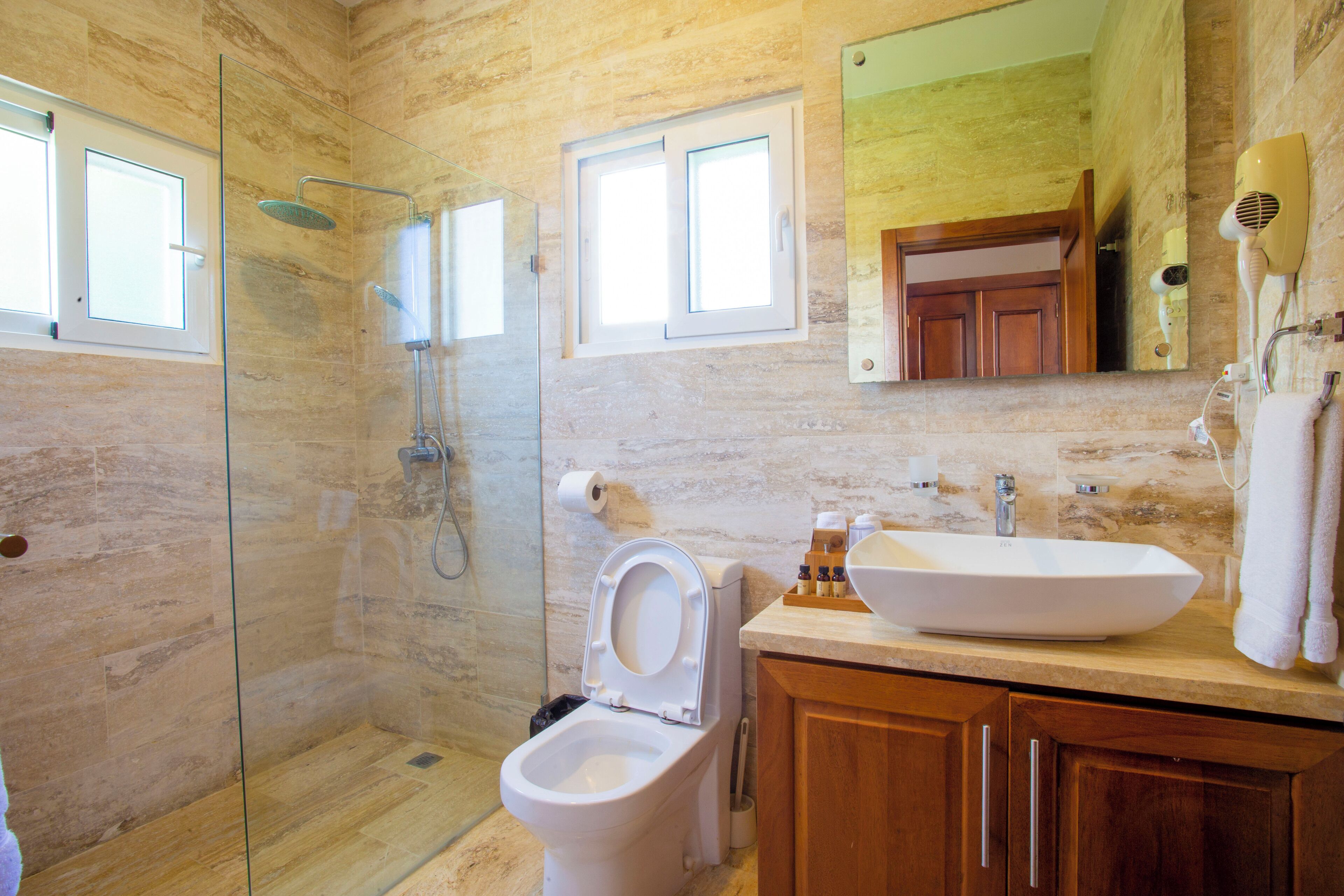 Een badkamer met een douchecabine van glas, toilet, wastafel, houten kastjes en een spiegel.