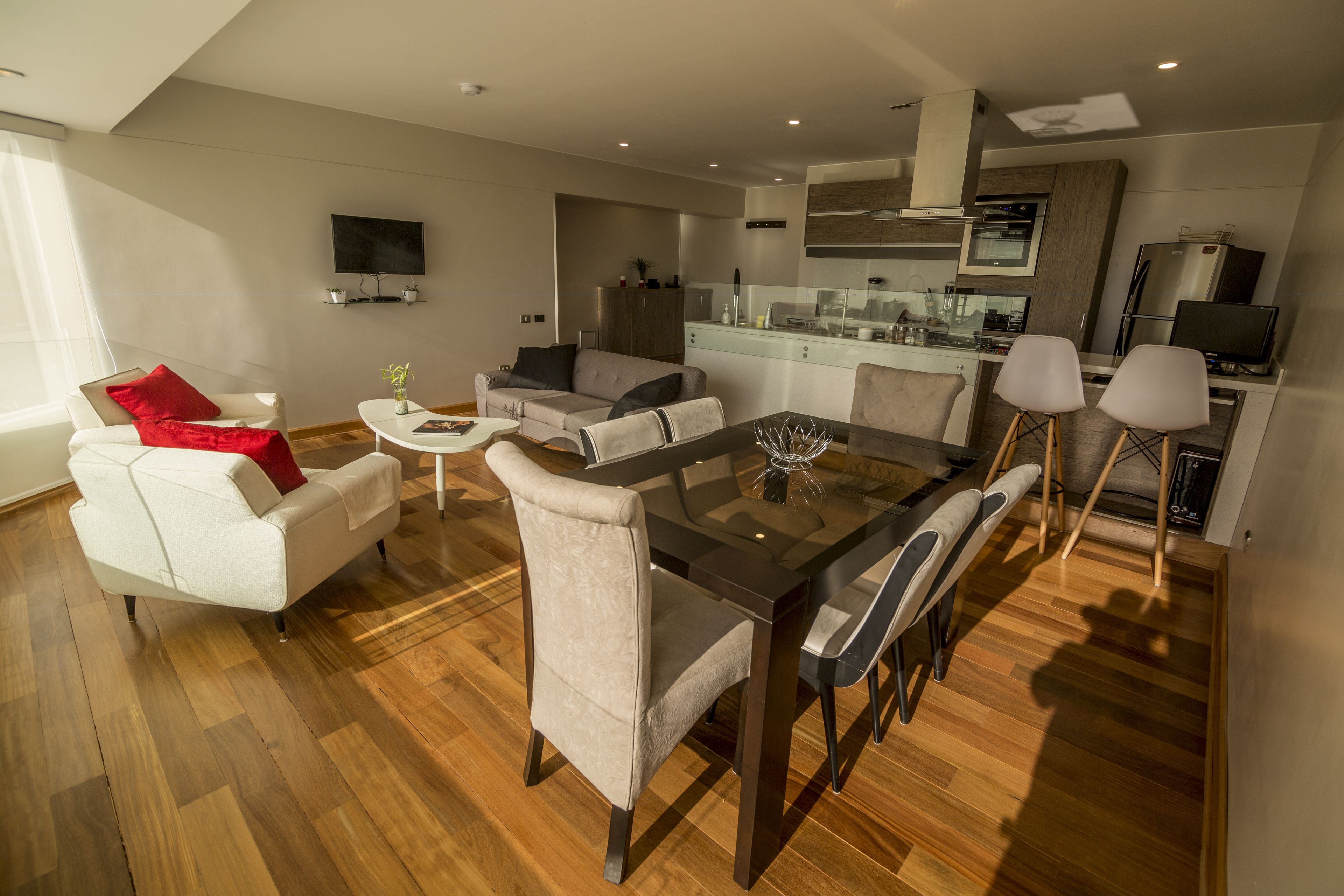 A modern living room with a dining area, a kitchen, and a TV mounted on the wall.
