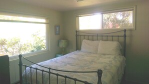 Un dormitorio con estructura de cama metálica, ventana con vista a árboles y lámpara de noche.