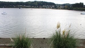 Una propiedad frente al agua con un césped que conduce a un muelle, rodeada de agua y colinas distantes.