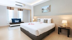 Una habitación de hotel moderna con una cama grande, un sofá, una mesita de noche con lámpara y un cuadro en la pared.