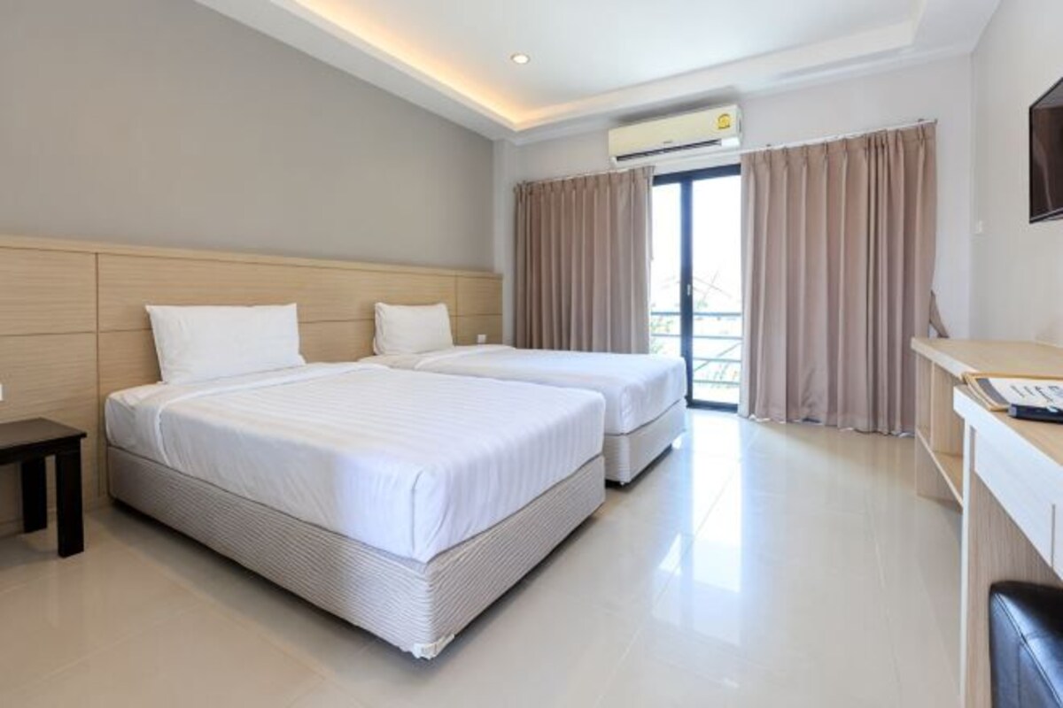 Habitación de hotel con dos camas, un escritorio y un ventanal grande con cortinas.