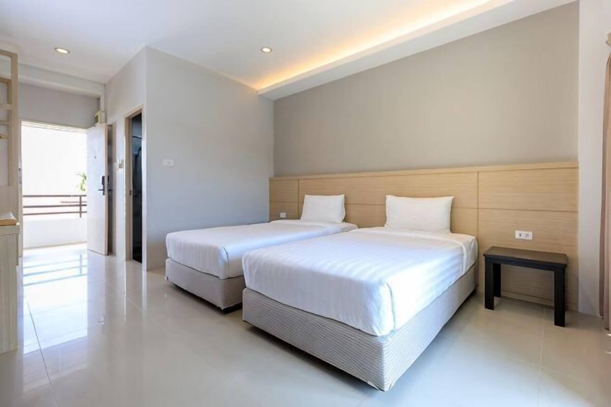 Una habitación de hotel moderna con dos camas, un cabecero de madera, una mesita de noche pequeña y vistas al exterior.