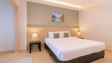 A modern hotel room with a large bed, two bedside tables with lamps, a painting on the wall, and a patterned rug on the floor.