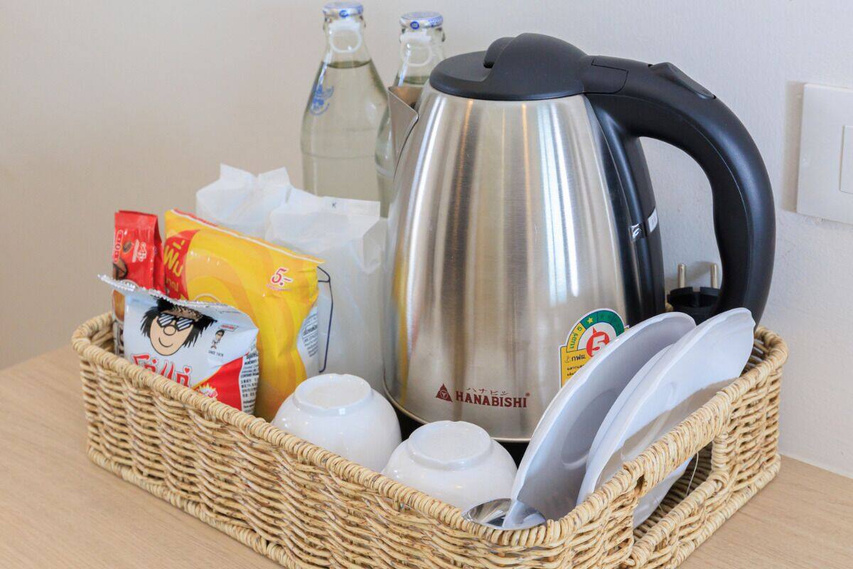 Una cocina con una tetera de acero inoxidable, una cesta de mimbre con alimentos y algunas botellas.