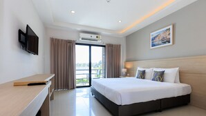 Habitación de hotel con cama, escritorio, televisor, equipo de aire acondicionado y balcón con cortinas.