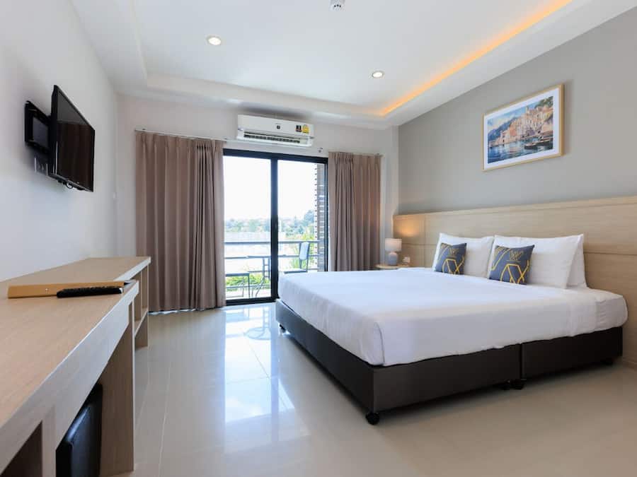 A hotel room with a bed, a desk, a TV, an air conditioning unit, and a balcony with curtains.
