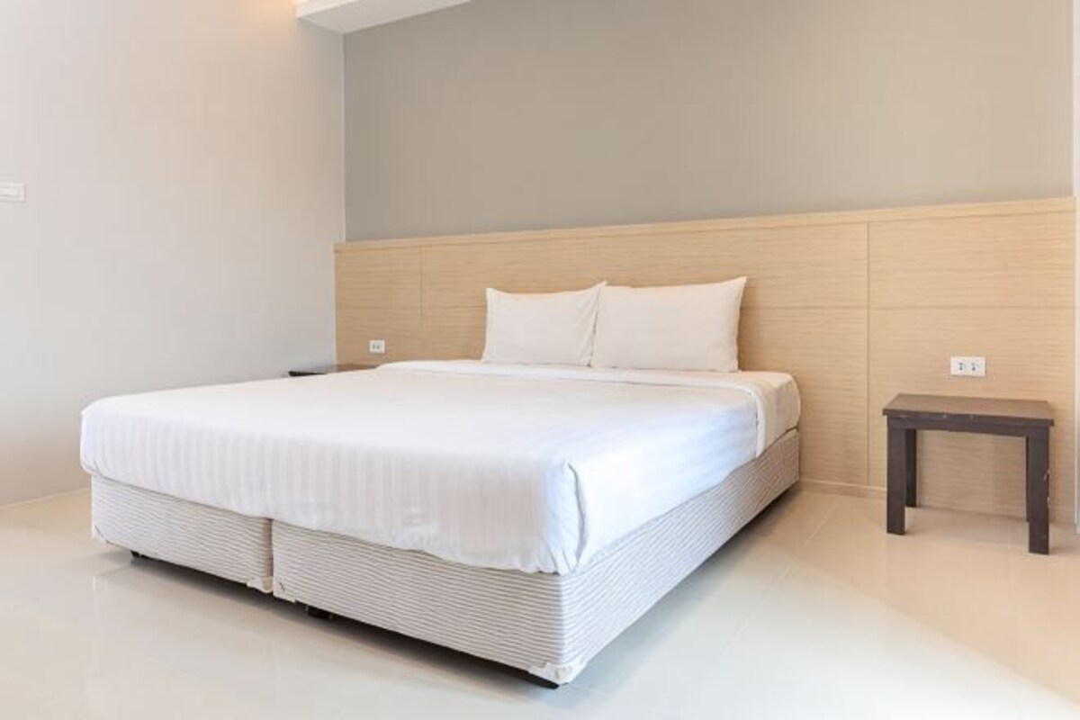 Una habitación de hotel moderna con una cama grande, cabecera de madera, mesita de noche pequeña y pared de color claro.