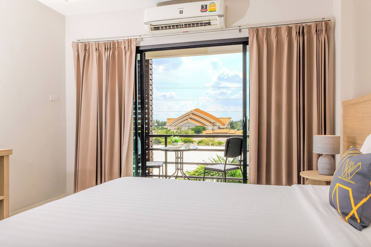 Habitación de hotel con cama, una mesa, una silla, aire acondicionado y vista a un edificio.