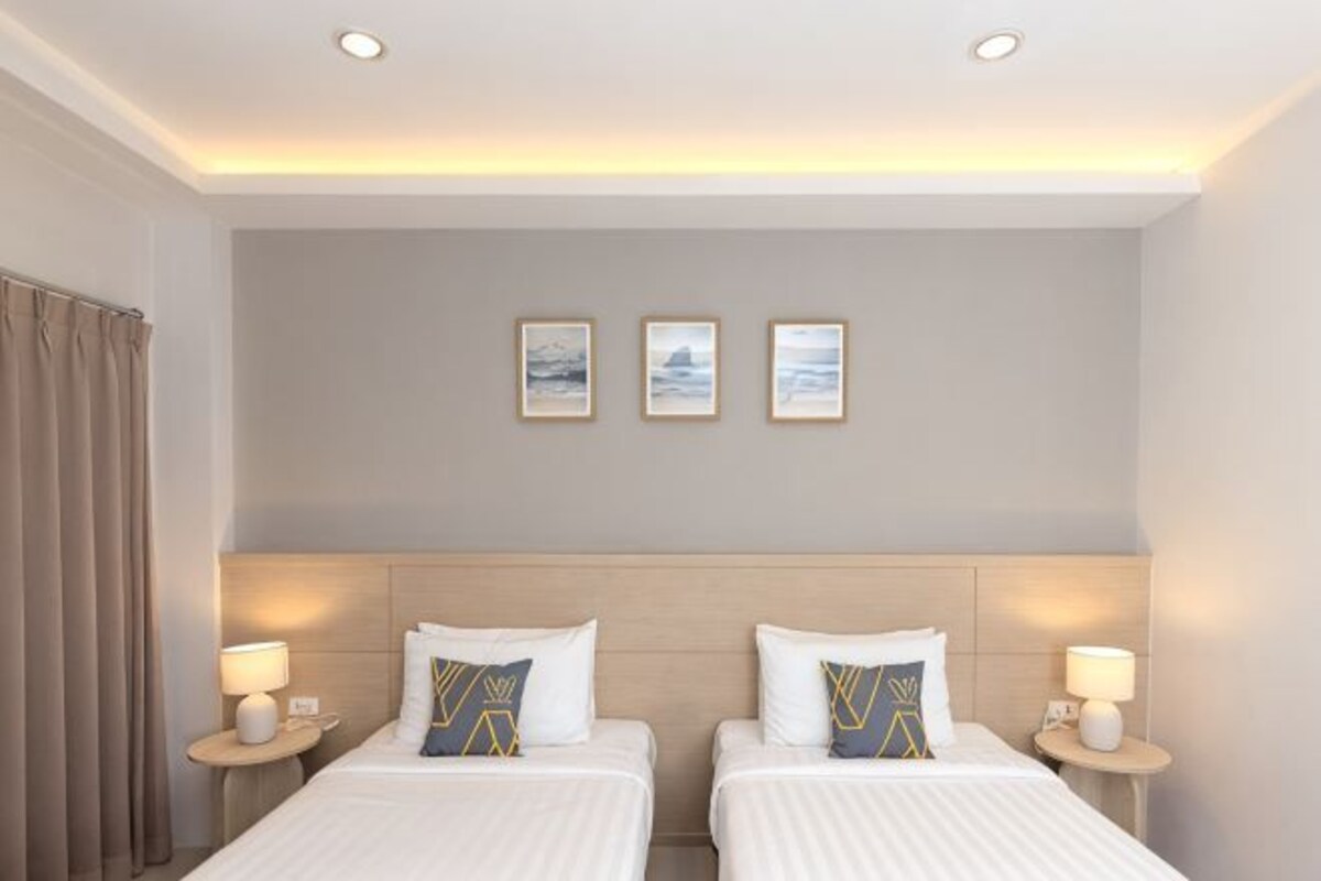 Habitación de hotel con dos camas, cabeceros, lámparas de noche y tres cuadros en la pared.