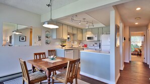 A modern kitchen with a central island, wooden dining table, and chairs.
