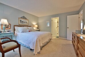 A bedroom with a bed, bedside tables, a chair, a dresser, and a door leading to another room. - Mutiny Bay Condo (Freeland)
