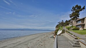 A beachfront property with a sandy beach, a clear view of the ocean, and a row of two-story houses with balconies.