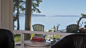 A view from a room with a large window overlooking a lake, featuring a chair, a small table with books, and a bottle.
