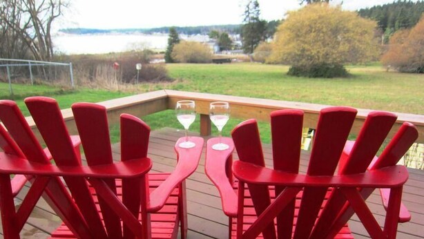 A deck with red Adirondack chairs and a table with two wine glasses. - Mutiny Bay Cottage (Freeland)