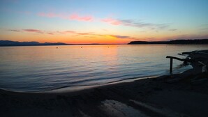 A beach with a wooden walkway leading to the water, calm sea, and a sunset in the background. - Mutiny Bay Cottage (Freeland)