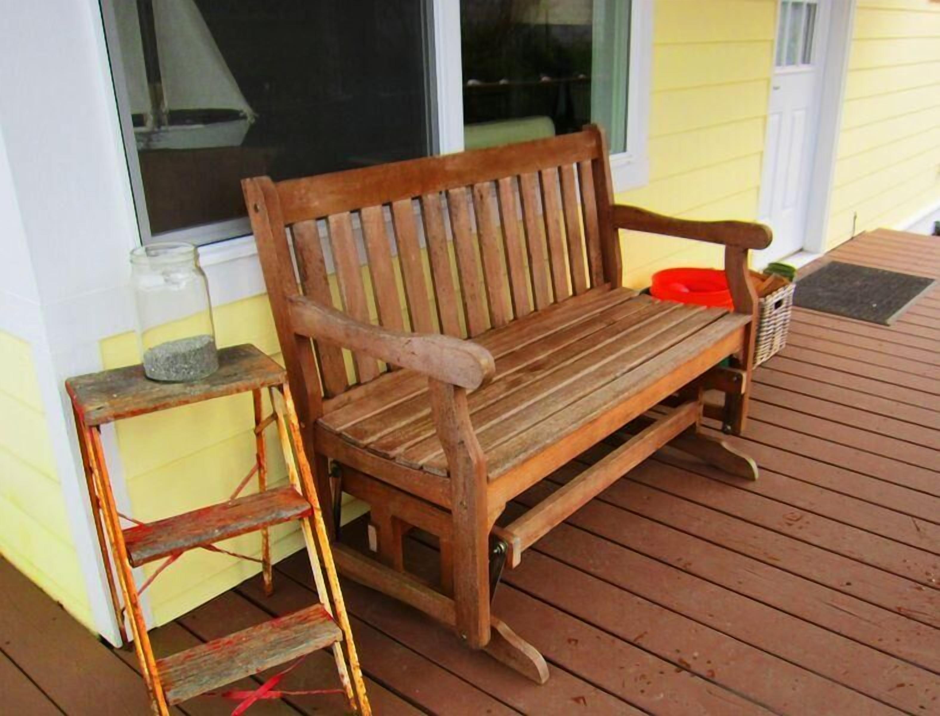 A wooden bench on a wooden deck with a small table and a ladder beside it.