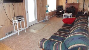 Ein gemütliches Wohnzimmer mit Fernseher, einer Couch, einem Kamin und einer Tür, die nach draußen führt.