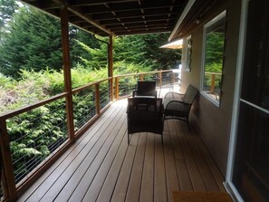 A wooden deck with a railing, two wicker chairs, and a view of dense greenery. - Eagles Watch (Coupeville)