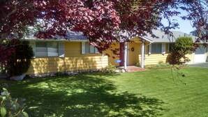 A yellow single-story house with a front porch, a well-maintained lawn, and a tree with red leaves. - 6th Street Langley Vacation House (Langley)