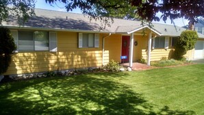 A yellow single-story house with a red front door, a small porch, and a number 218 sign. - 6th Street Langley Vacation House (Langley)