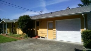 A single-story yellow house with a white garage door, a chimney, and a small front porch.