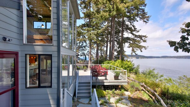 Ein modernes Haus mit einer Terrasse, die auf einen See blickt, mit einem Kiesweg und einer Holztreppe.