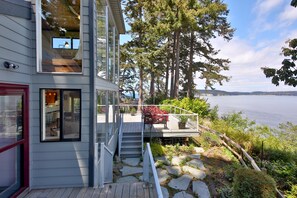 A modern house with a deck overlooking a lake, featuring a stone pathway and a wooden staircase.