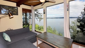 Ein Zimmer mit großem Fenster und Seeblick, Deckenventilator und einer Couch mit Lampe.
